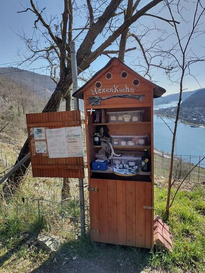 Ein kleiner Selbstbedienungsladen in Form eines kleinen Häuschens. Die Tür steht offen und innen stehen verschiedene Marmeladen, Gin, Magnete und einiges mehr .