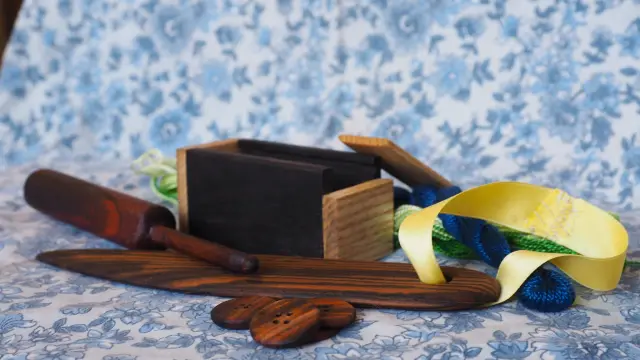 Des petits objets en bois disposés sur un tissu floral. Il y a un crochet, une boite, un long objet plat et fin (le plioir) et des boutons. Tous les bois sont différents, avec des nuances très intenses.