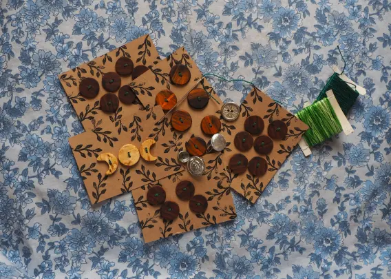 Pleins de plaques de boutons disposées dans un décor. Ce sont des boutons en bois de différentes couleurs cousues sur une petite carte de craft.
