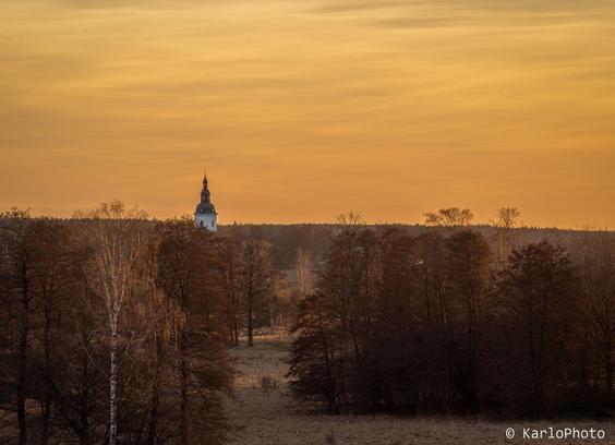 A church in the distance, surrounded by trees. Moody sunset lighting.