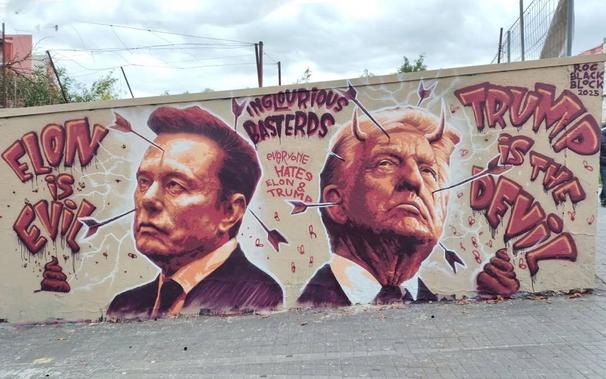 A politically charged mural by street artist Roc Blackblock in Barcelona, Spain, featuring portraits of Elon Musk and Donald Trump. The artwork, painted in a reddish monochrome palette, portrays Musk in a suit with the words "Elon is Evil" to his left, while Trump, depicted with devil horns, is accompanied by the phrase "Trump is the Devil" on the right. The center of the mural includes the phrase "Inglourious Basterds" and "Everyone Hates Elon &amp; Trump." The piece incorporates satirical elements like arrows piercing both figures and small icons such as flies and excrement, enhancing its critical tone. The mural is signed "Roc Black Block 2025."