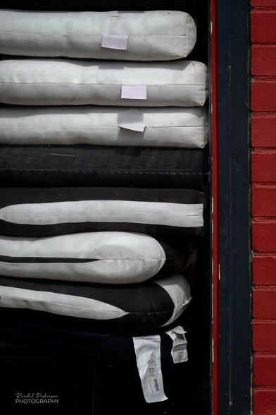 Black and white outdoor seat cushions are stacked on the opposite side of a window waiting for the restaurant's outdoor seating area to open in the spring.