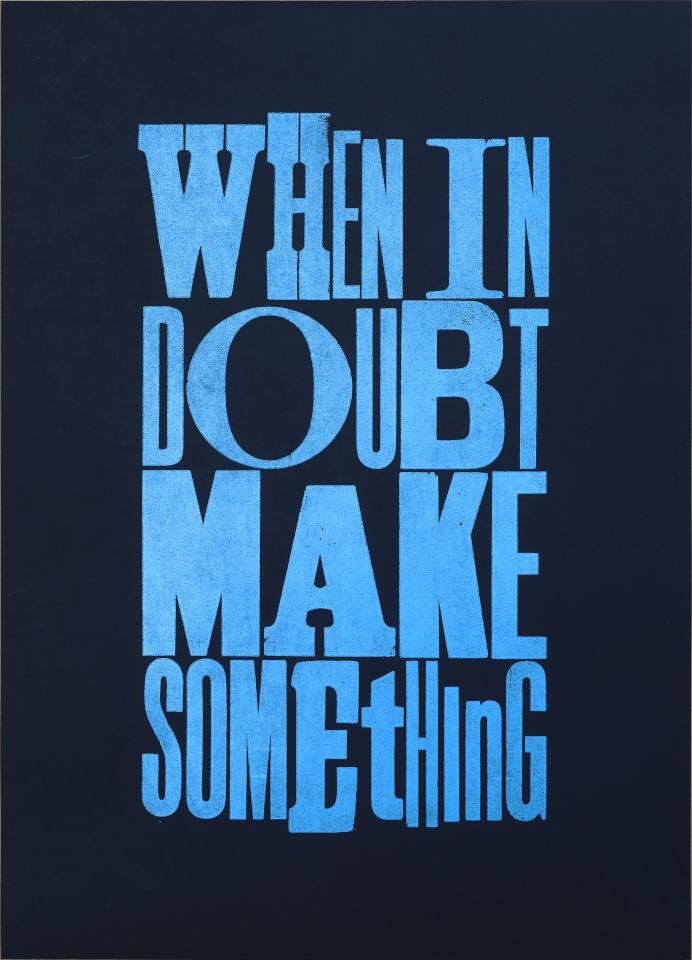 A handprinted poster with the text When in Doubt Make Something in bright blue ink on black paper. The letters are a mishmash of old wood type. The text is arranged such that it creates a rectangular shape.