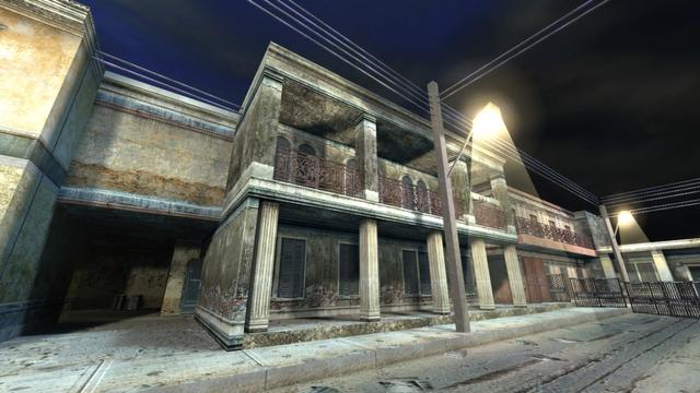 In this picture you can see several houses. And a road. In addition, two street lamps. On the right, the road is blocked off with metal fences. You can see an underpass on the left and an open house entrance on the right. The house with the open entrance has balconies that are held in place by concrete pillars. This is on the map cs_havana in the game Counter-Strike 1.6.