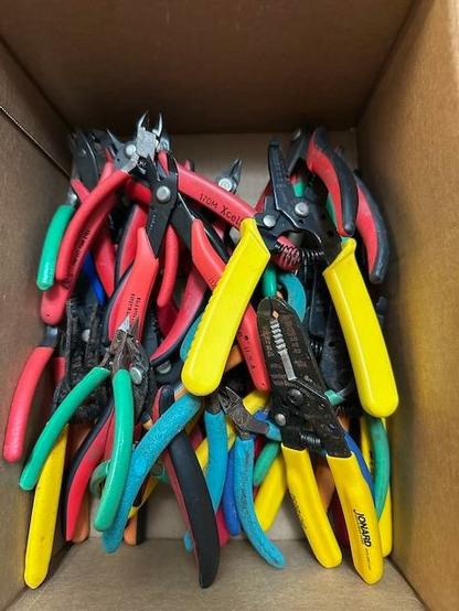 A box of around two dozen pairs of electronic nipper and wire stripper tools.