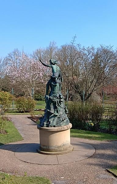 A bronze statue of Peter Pan sitting atop a tree stump in Sheffield Botanic Gardens.