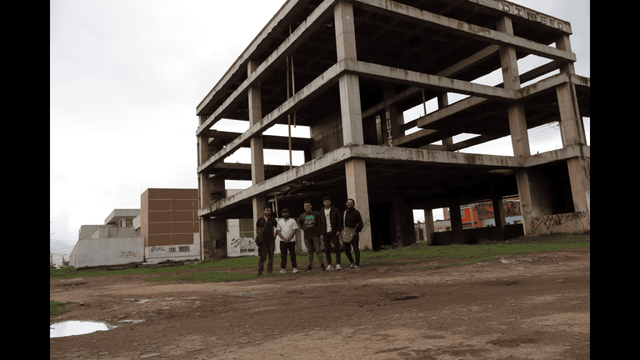 En la imagen aparecen los integrantes de Albert Opina y de Lente Tisquesusa. Detrás de ello se encuentra una estructura tétrica que sería mega biblioteca pero no pudo ser por la corrupción de los líderes locales