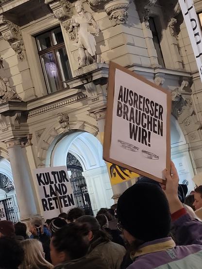 Ausschnitt der Demonstration vorm Rathaus, jemand hält ein Schild: "AUSREISSER BRAUCHEN WIR" und etwasvweiter weg: "Kulturland retten"