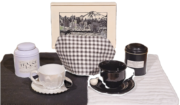 Tea tableau divided in stark black and white with one side as the reverse of the other, utilizing contrasting china, linens, and tea tins. There is also a woodcut image of Seattle in the background.