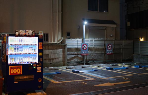 A lonely parking space in a Tokyo backstreet, a single lamp illuminates the liminal space, its only companion a buzzing brightly lit vending machine, standing sentry.