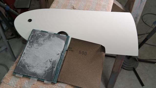 A small glider part (battery box cover) has been sanded to remove orange peel. The finish is now matte. I have made some test pads of foam rubber, double sided tape, and various grades of sandpaper. Working with bright light helps me evaluate my progress and surface quality.