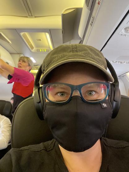 Me on the plane on the way to Sydney. I m wearing a hat, headphones and a black mask.