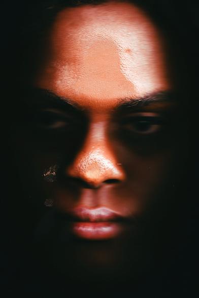 A close-up portrait of the photographer, featuring strong contrasts between light and shadow. The skin texture and facial features are highlighted, with a serene yet intense expression.