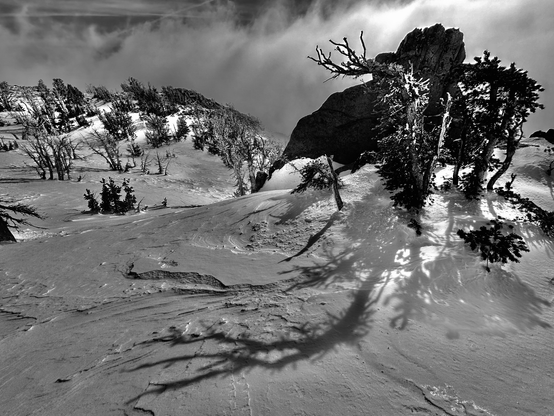 The late afternoon sun shines through the clouds on the snow covered slope of Fawn Ridge, laying shadows against the rippled snow covered surfaces of the mountain.