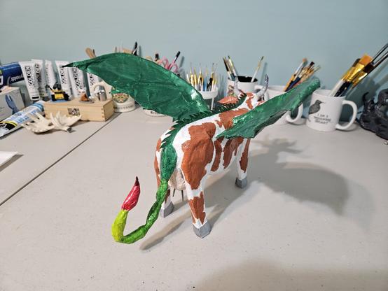 Back view of the Guernsey cow-dragon.  It's green, leathery bat wings are visible, as its scorpion tail.