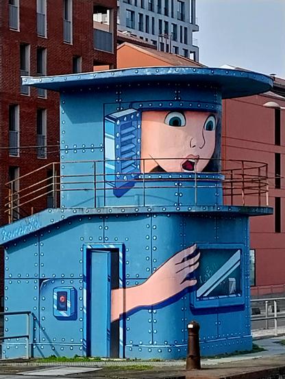 Bâtiment bleu, contrôle d'une écluse à Bordeaux, qui sert de support à une oeuvre de StreetArt. Un visage sort d'une fausse fenêtre, et une main de la porte d'accès au bâtiment.