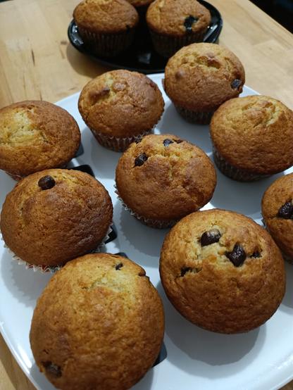 Photo de muffins bien dorés et dodus rangés sur une assiette blanche. En arrière plan on aperçoit une seconde assiette, noire cette fois, avec quelques muffins de plus.