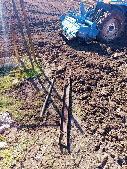 A bunch of things the rotavator revealed, including a pipe, a bit of plastic on the left and a big steel C-beam covered in soil. The rear of a blue tractor with rotavator is visible in the freshly tilled field behind.