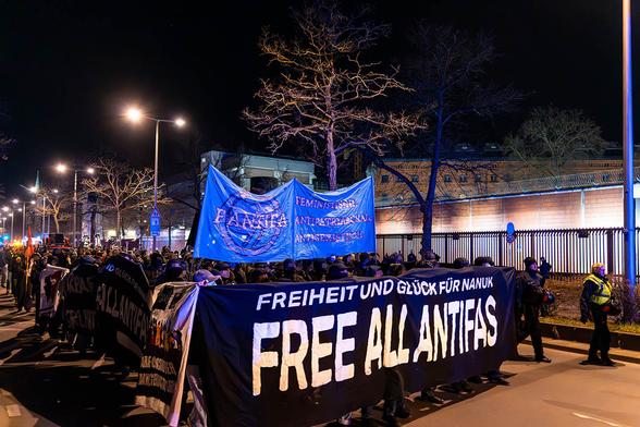 Das Foto von © Björn Obmann zeigt einen Blick auch die Demo vor der JVA Moabit, das Fronttransparent "Freiheit und Glück für Nanuk - Free all Antifas". Dahinter das Hochtransparent der FAntifa sowie der Text "Feministisch - Antipatriarchal - Antisexistisch" sowie weitere Seitentransparente und zahlreiche Menschen.