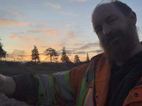 A COs white male with a large red beard offers out a hug. He wears a reflective jacket. He wishes the work day would just be over with