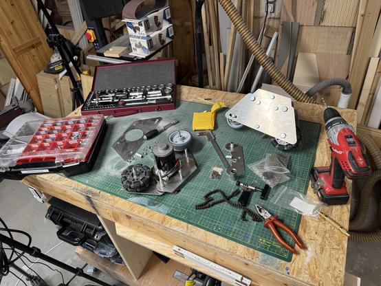 My workbench filled with various tools like pliers, a drill and socket wrench. Also a case of machine screws and nuts and bolts. In the middle the disassembled drive of Artoos foot. The assembled drive for reference stands in the back.