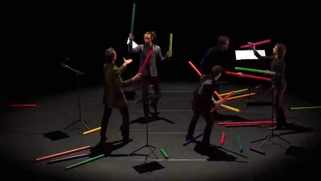 Four musicians perform on a dark stage with colorful illuminated tubes instead of traditional instruments, creating a unique visual and musical performance art piece.