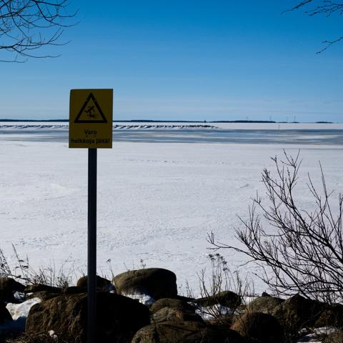 A view from seashore, on ice-covered waters, with a warning sign saying "beware of thin ice" in Finnish.