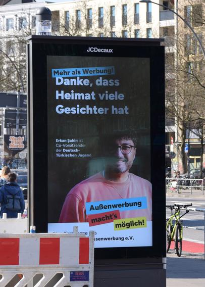 Ein Werbebildschirm an einer Straße mit der Botschaft "Danke, dass Heimat viele Gesichter hat".