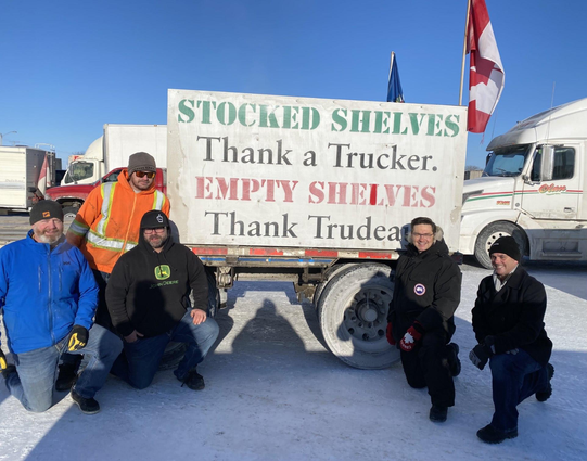 Pollievre posing for a picture with trucker convoy supporters in front of a sign reading: "Stocked Shelves, Thank a Trucker. Empty Shelves Thank Trudeau."