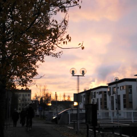 Late autumn golden hour in the Oulu waterfront, beside a canal, with a bridge and apartment buildings in the background.