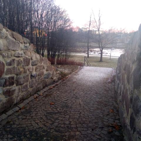 Late autumn photo of cityscape, with park walkway going through old castle walls, with park and river seen behind.