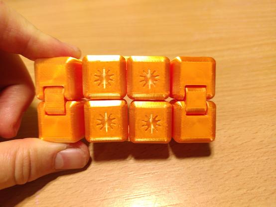 Nahaufnahme eines 3D gedruckten  Infinity Cubes, ein Fidget Spielzeug das aus 2x4 zusammenhängenden Würfeln besteht. Es ist hellorange, die 4 Würfel in der Mitte haben jeweils ein kleines Sonnensymbol in der Mitte.