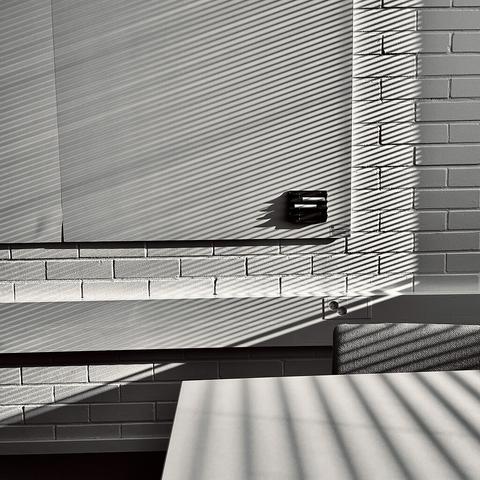 Black and white image showcasing geometric shadows cast on a textured wall and table by illuminated blinds, creating a stark contrast.