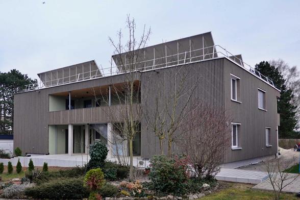 Ein zweistöckiges Holzhaus mit Flachdach, auf dem Solarthermiemodule stehen.