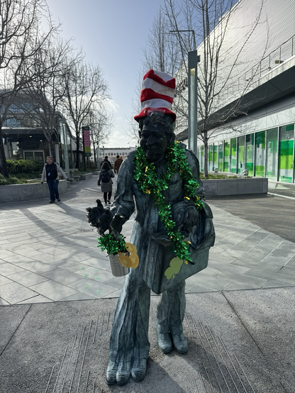 Statue of a salesman with multiple hands and feet. Decorate with Waldo hat and green st Patrick’s day garlands.