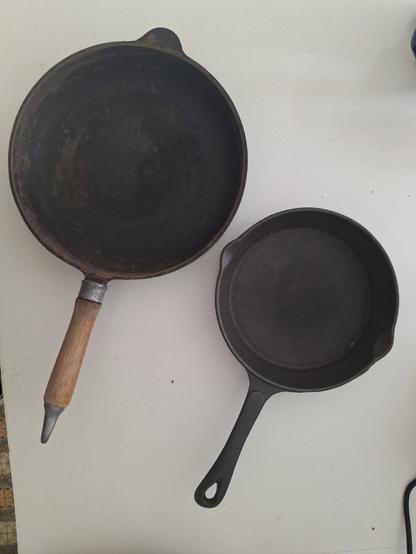 Two cast iron frying pans of different sizes on a white bench.