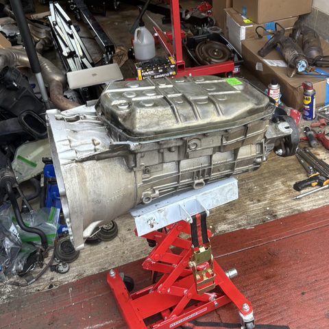 The fully reassembled transmission sits on a transmission jack, its newly cleaned and reinstalled oil pan facing up.