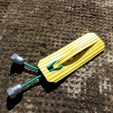 Rectangle de lance à incendie jaune dans lequel est découpée une fente.
En-dessous de la fente, un trou carré.
Dans la fente et dans le trou passe une paracorde verte dont les bouts sont scellés par des écrous borgnes trop gros pour passer dans le trou.