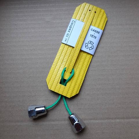 Rectangle de lance à incendie jaune dans lequel est découpée une fente.
En-dessous de la fente, un trou carré.
Dans la fente et dans le trou passe une paracorde verte dont les bouts sont scellés par des écrous borgnes trop gros pour passer dans le trou.