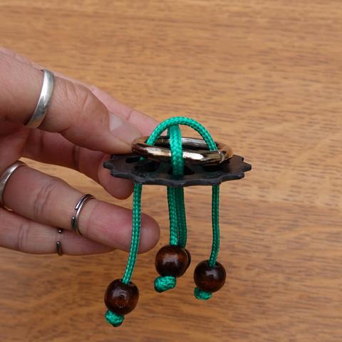 Casse-tête composé d'un galet de dérailleur dans lequel passe de la paracorde entrelacée, qui retient un anneau en metal au-dessus du galet.