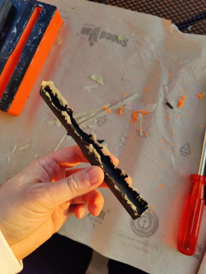 The carbon part after demoulding. The edges are rough where the excess resin escaped during mould closure. Some carbon fibres also tried to exit the mould through the parting line. The female part of the mould is visible on the side.