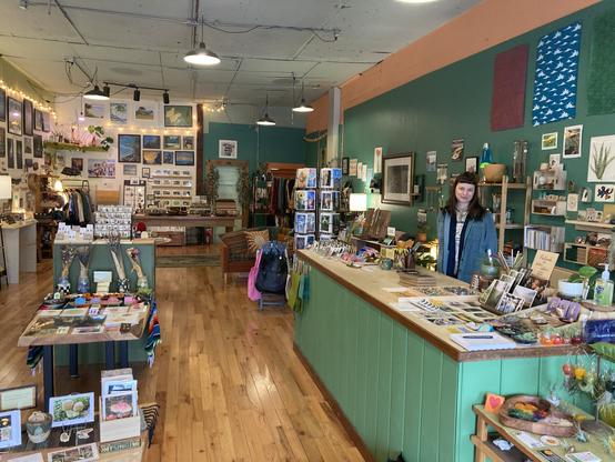 Photograph of the interior of Good Day shop in Arcata, CA, with the owner/operator Marta behind the counter. The room features artwork, jewelry, prints, pottery, glass, and various other art pieces and crafted items made by Humboldt County residents.