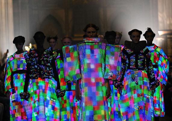 Several models walk the runway in dramatic, multicolored LED-lit garments.