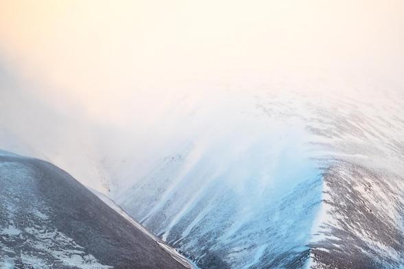 In the high Arctic realm of Svalbard, where the sun's touch is fleeting and the cold whispers secrets to those who listen, this image captures a moment where time itself seems to pause. The vast expanse of snow and ice stretches infinitely, merging with a sky that holds the soft hues of dawn or dusk—it's hard to tell which, as the polar day and night dance their endless waltz. Jagged mountain peaks punctuate the horizon, standing as silent sentinels to an untouched wilderness. The photograph invites the viewer into a world where solitude is profound, and the beauty lies in the delicate balance between harshness and serenity.