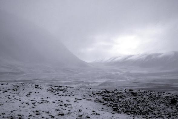 In the high Arctic realm of Svalbard, where the sun's touch is fleeting and the cold whispers secrets to those who listen, this image captures a moment where time itself seems to pause. The vast expanse of snow and ice stretches infinitely, merging with a sky that holds the soft hues of dawn or dusk—it's hard to tell which, as the polar day and night dance their endless waltz. Jagged mountain peaks punctuate the horizon, standing as silent sentinels to an untouched wilderness. The photograph invites the viewer into a world where solitude is profound, and the beauty lies in the delicate balance between harshness and serenity.