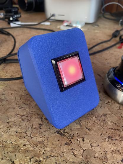 A royal blue 3D printed tapering box. The front of the enclosure has a single clicky button with a not-at-all ominous glowing red LES
