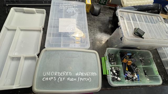 Various plastic compartment boxes from as many brands and reuses as come to me. White paint marker declares some to be "unordered harvested chips (by form/pitch)", and others "alphabetized harvested chips (usable)". Most are clear plastic and within those are mini-mountains of pre-loved electronic waste, divided into their smallest reusable form.