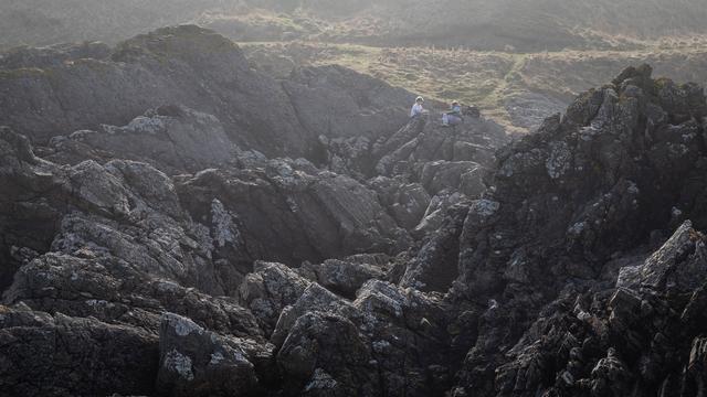 A hazy photograph of a grey, rocky landscape. You can just about make out a couple of kids sat chatting on the rocks.
