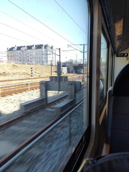 View fromma train window of a blurry track and a large grey building with turrets at the side of the track in Copenhagen