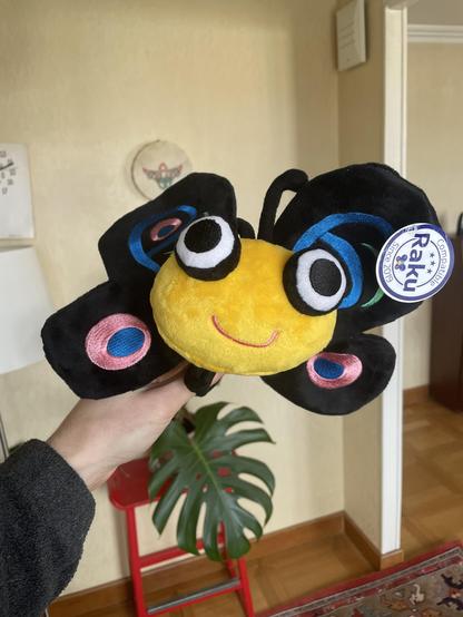 A toy plush animal. It’s a yellow butterfly that smiles. It got black wings with pink, blue and green embroideries.